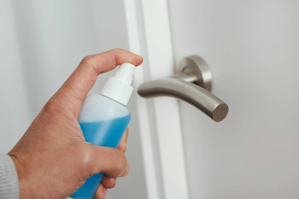 closeup of a caucasian man disinfecting the door handle by spraying a blue sanitizer from a bottle